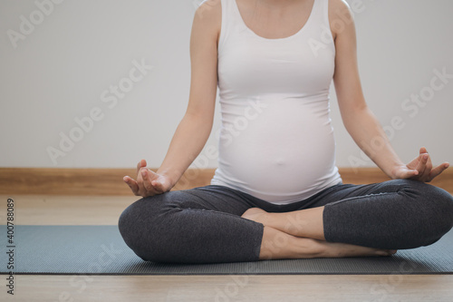 Calm pose young asian pregnant woman practice yoga in the lotus position for pregnant to meditation and exercise on mat for wellbeing while rest at home.lll