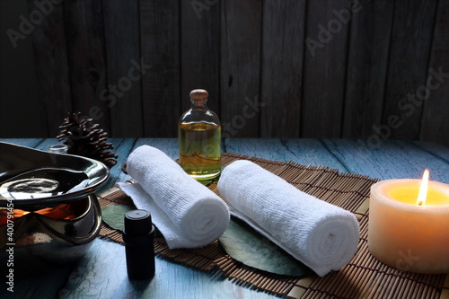 white clean cotton spa towel cloths prepared for day spa service on blue wooden tabel with massage oil bottle, essential oil, candle, and oil burner with background of vintage wooden wall in spa