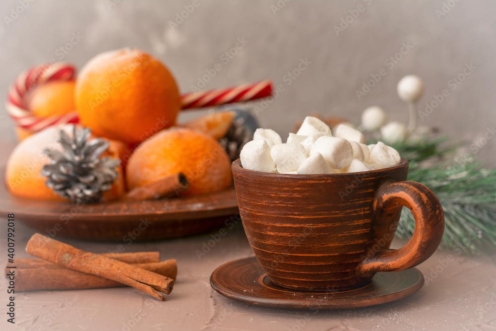 Fototapeta premium Hot coffee with marshmallows in clay cup on table. Tangerines, cinnamon and candy in winter composition. Selective focus, blurred background