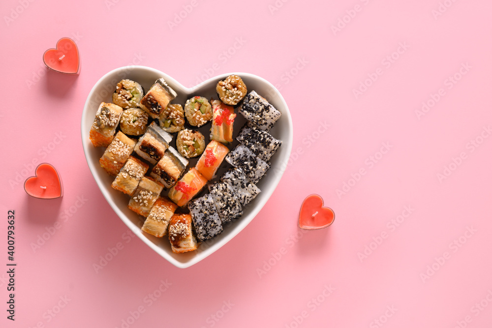 Sushi set in plate as heart on pink background decorated romantic candles. Valentine's day. Space for text. Food delivery. Sushi set in plate as heart on pink background decorated romantic candles. Valentine's day. Space for text. Food delivery.