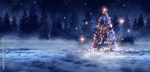 Night winter forest fantasy landscape with a Christmas decorated tree. Festive bokeh lights, dark forest, neon lights. Decorated Christmas tree in the night forest. Background for postcards. 