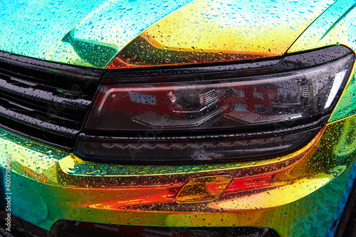Chameleon holographic colour car in the rain. Car wrapping with iridescent paint. Raindrops on the car. Front view closeup. Modern LED headlights. Car wrapping. 