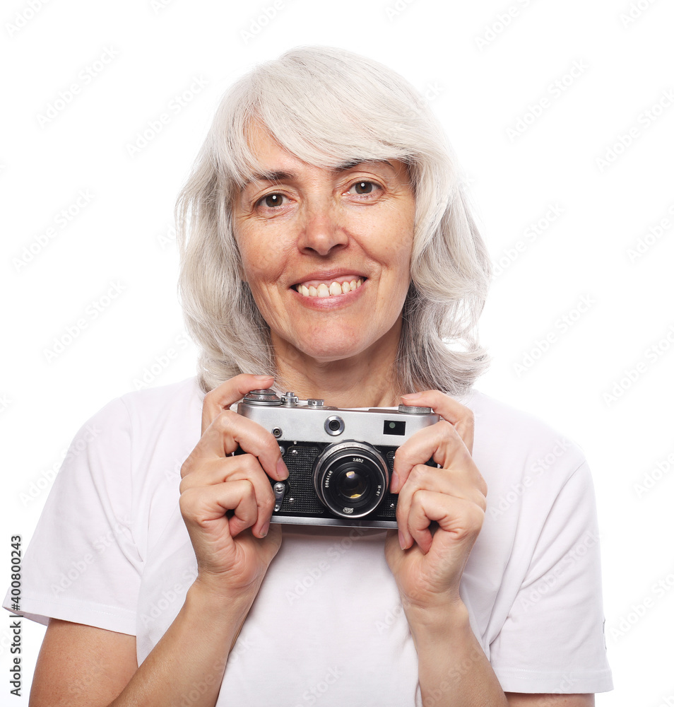 An elderly woman is holding a camera and smiling. The pensioner works as a photographer and enjoys life. An elderly woman is holding a camera and smiling. The pensioner works as a photographer and enjoys life.