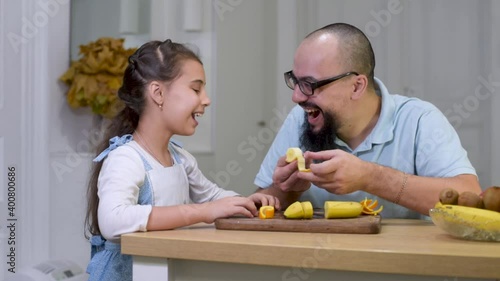 Dad feeds a girl a banana in the kitchen, Food for children. Berries and fruits.