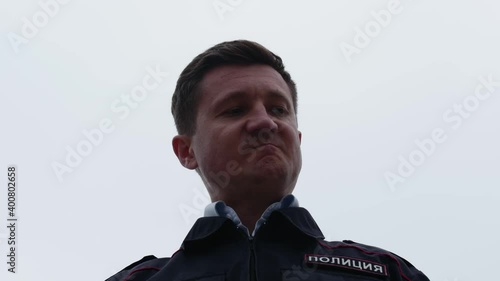 Close up portrait of a man in a police uniform against a white sky background.