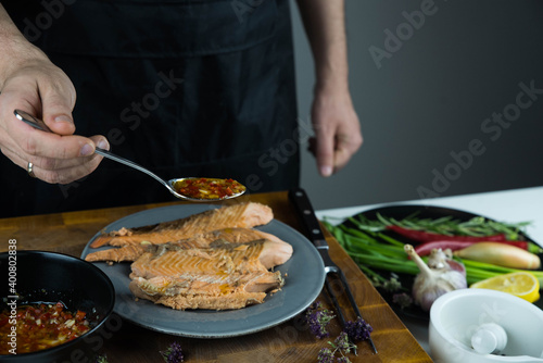 Chief cook is seasoning with chili sauce carved fish baked in salt crust. Seafood cooking. Salmon or seabass under salt crust with vegetables. © strigana