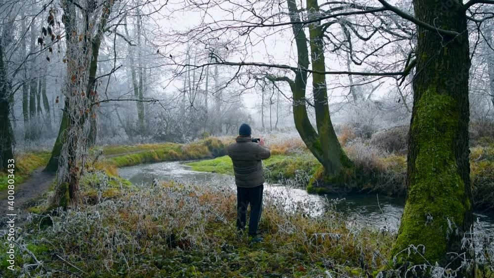 Man resting and taking photos in the park among green, frozen grasses and branches. Natural park landscape in early winter morning. Man resting and taking photos in the park among green, frozen grasses and branches. Natural park landscape in early winter morning.