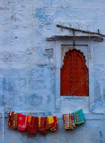 Red window on blue wall, in Jodhpur, where several saris are hung