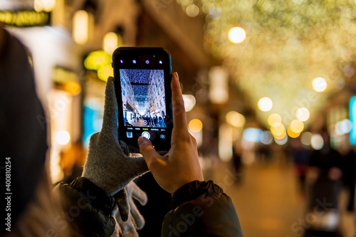 Photography Selective focus of a girl taking a photo with her phone of a festive street deco