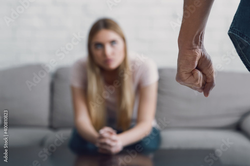 Obraz na płótnie Man with fist close up, and sad woman sits at table in living room interior