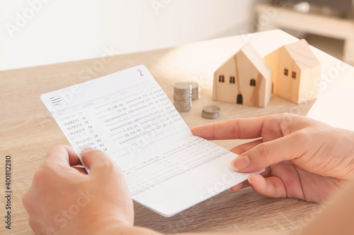 Hands holding account book bank with stack of coins and house model on wooden table. Selecitve focus. Saving, real estate, home insurance and mortgage loan concept.