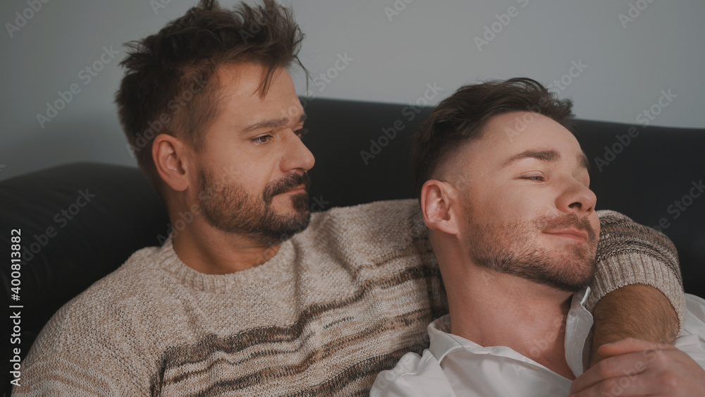 Fototapeta premium Young lovely gay couple cuddling and relaxing on the couch. Different family lifestyle concept Love and care. High quality photo