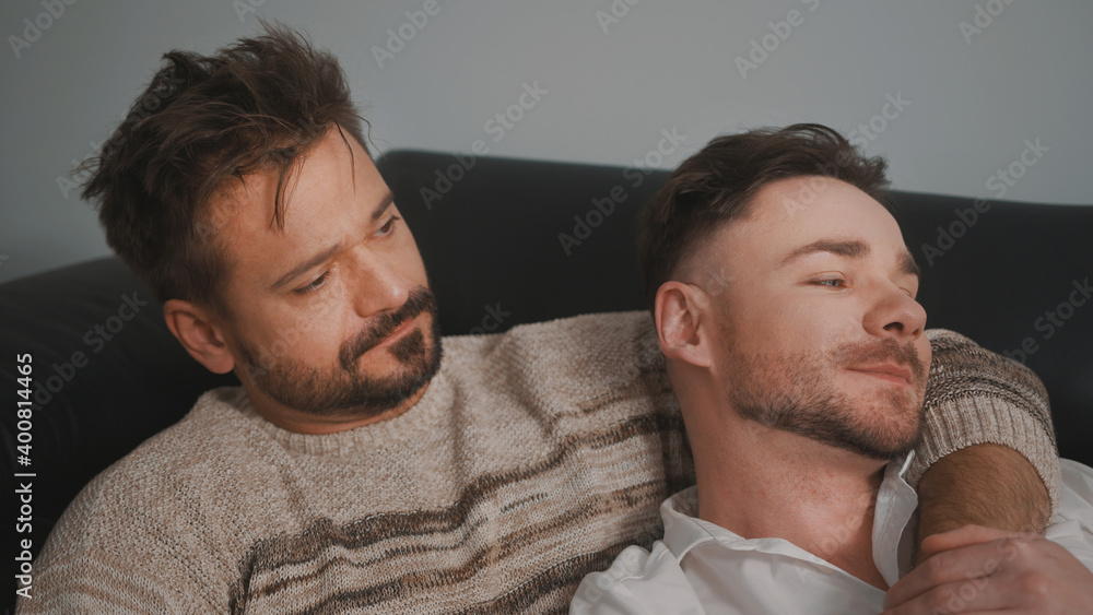 Fototapeta premium Young lovely gay couple cuddling and relaxing on the couch. Different family lifestyle concept Love and care. High quality photo