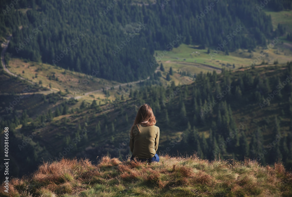 Girl sitting on grass against mountain valley