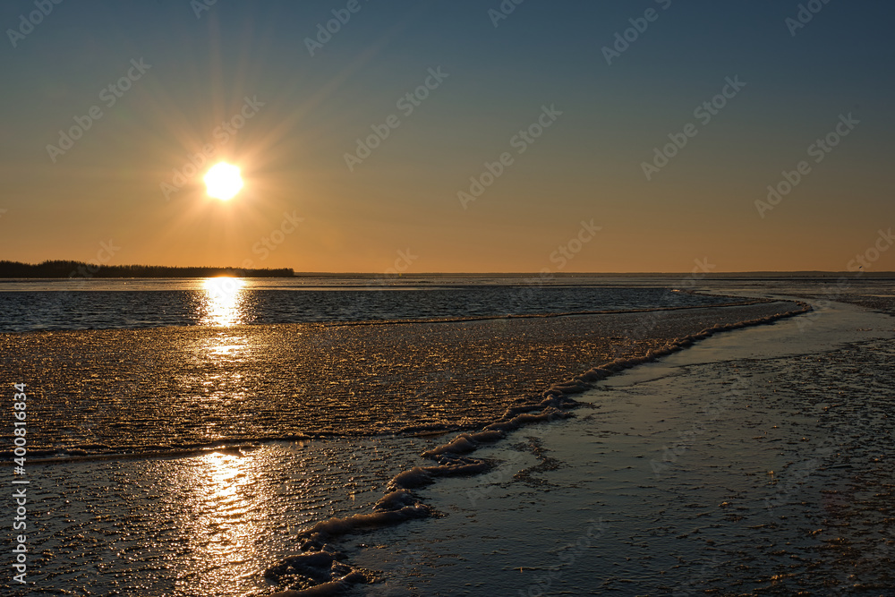 Fantastic colors of a winter water landscape at sunrise on a frosty morning. Open water is inexorably covered with dark ice, above - a bottomless sky and a bright yellow sun.