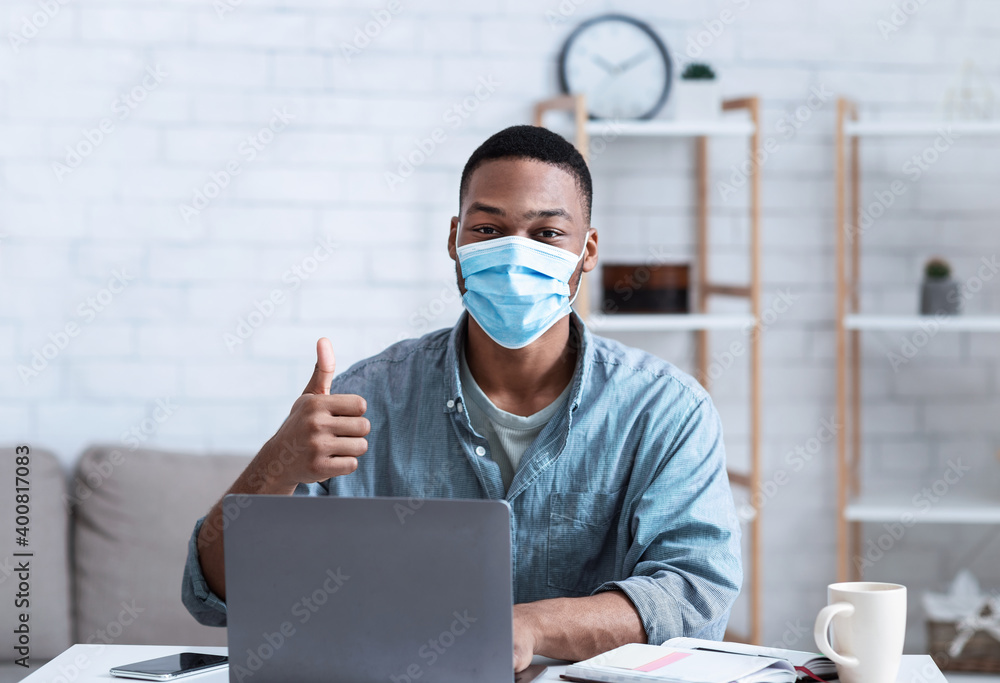 African Man Wearing Mask Sitting At Laptop Gesturing Thumbs-Up Indoor African Man Wearing Mask Sitting At Laptop Gesturing Thumbs-Up Indoor
