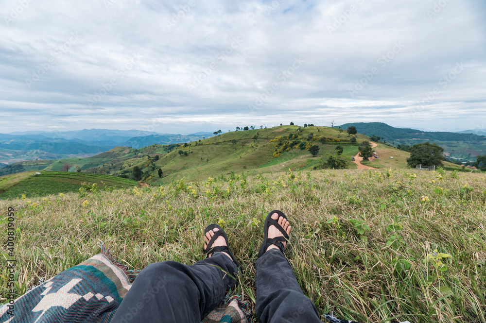 Legs of traveler relaxing on green hill in countryside