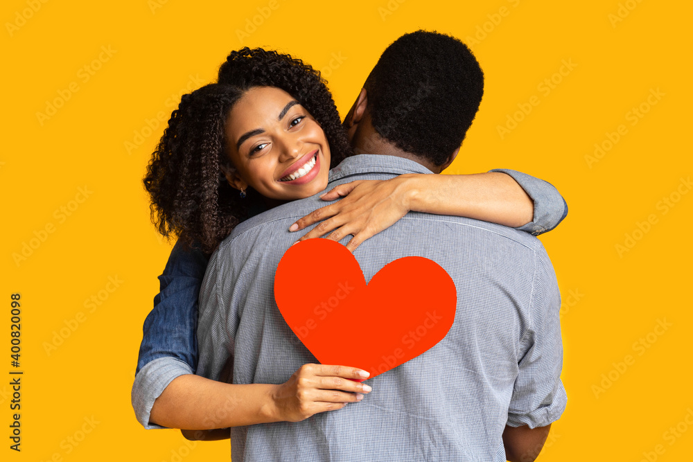 Happy african american woman in love hugging boyfriend and holding red heart