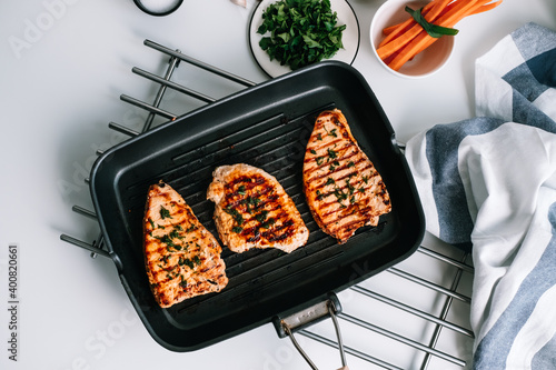 Grilled turkey steak with herbs and spices in black grill pan on the table.