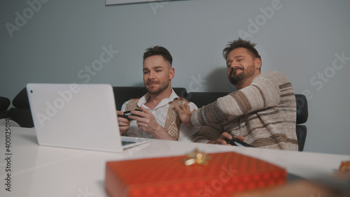Excited gay couple playing video games on laptop using joystic. High quality photo