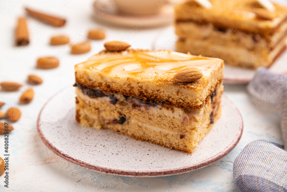 Honey cake with milk cream, caramel, almonds and a cup of coffee on a white concrete background. Side view, selective focus. Honey cake with milk cream, caramel, almonds and a cup of coffee on a white concrete background. Side view, selective focus.