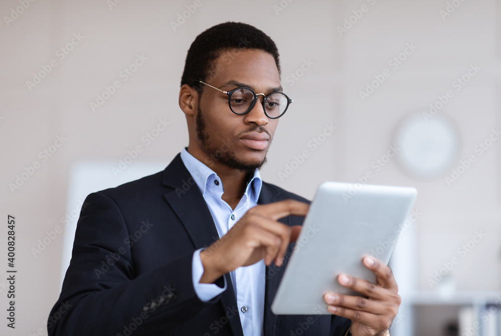 Serious black entrepreneur in glasses using digital tablet Serious black entrepreneur in glasses using digital tablet