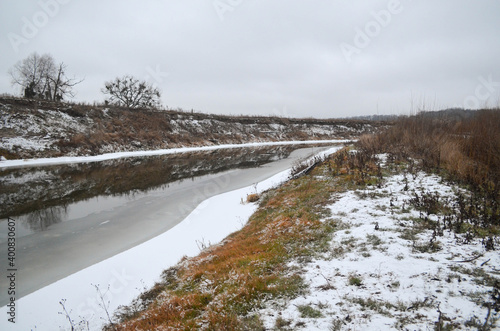 View on the river in winter. Grass covered with snow, northern scenery. Wild nature at wintertime.