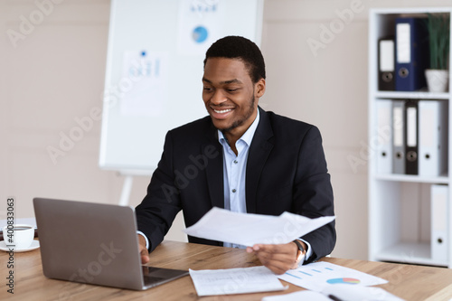 Happy black businessman checking reports in modern office