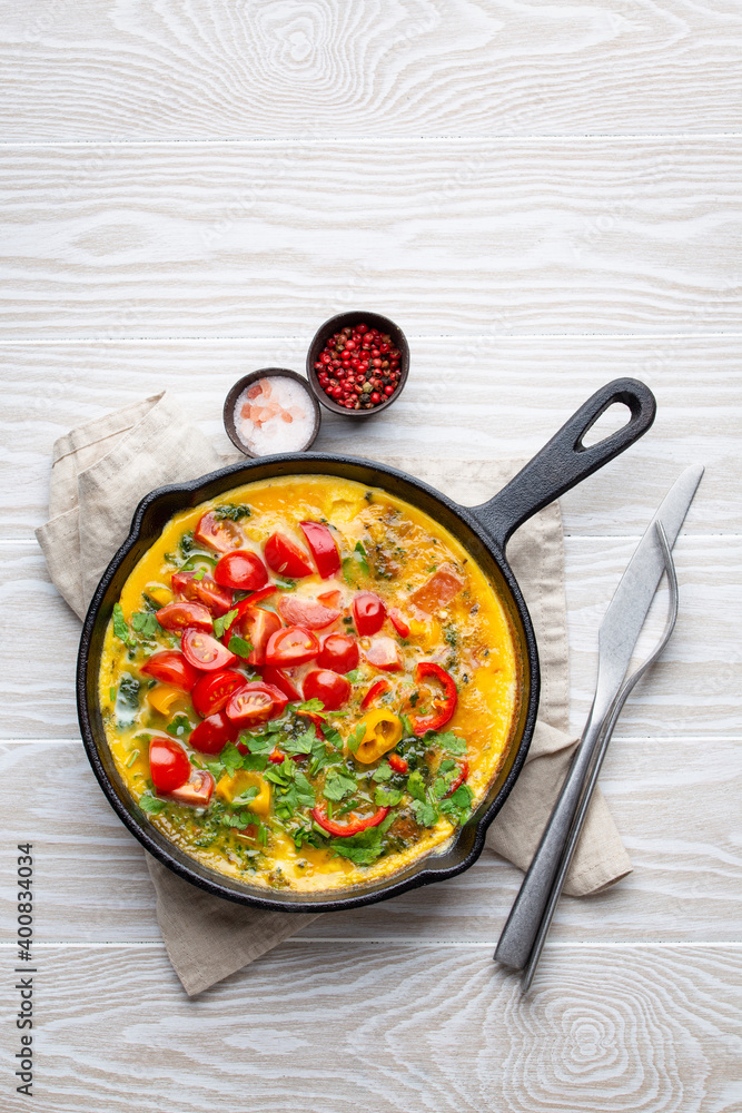 Healthy frittata in cast iron pan with fried beaten eggs and seasonal vegetables on white rustic wooden background. Italian omelette with organic spinach, bell pepper, tomatoes, from above Healthy frittata in cast iron pan with fried beaten eggs and seasonal vegetables on white rustic wooden background. Italian omelette with organic spinach, bell pepper, tomatoes, from above