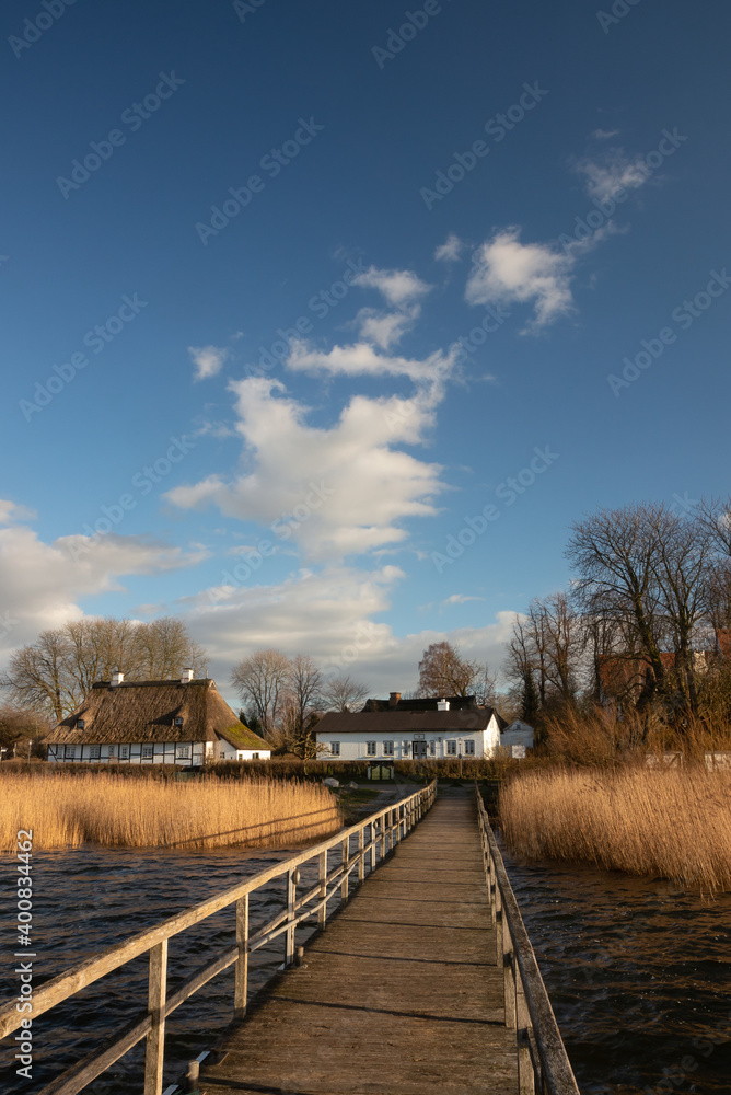 Fototapeta premium Idyllic view from a wooden jetty to the picturesque Sieseby village with old thatched country houses.