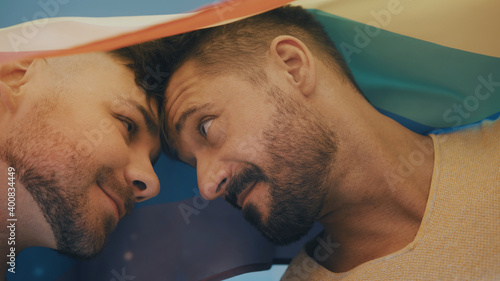 Portrait of two young handsome homosexual men covered with rainbow flag looking at each other. High quality photo photo