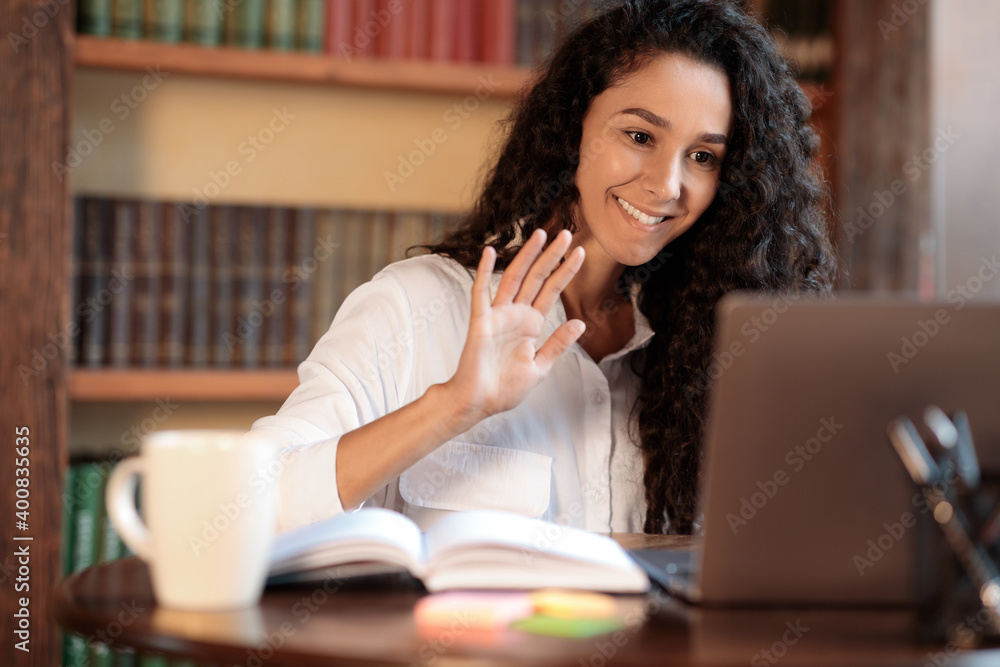 Woman sitting at desk, using laptop and waving to webcam Woman sitting at desk, using laptop and waving to webcam