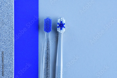 Winter toothbrushes concept. Gray toothbrush with snowflake with transparent shiny toothbrush on paper color block background. Selective focus. Health care concept. 