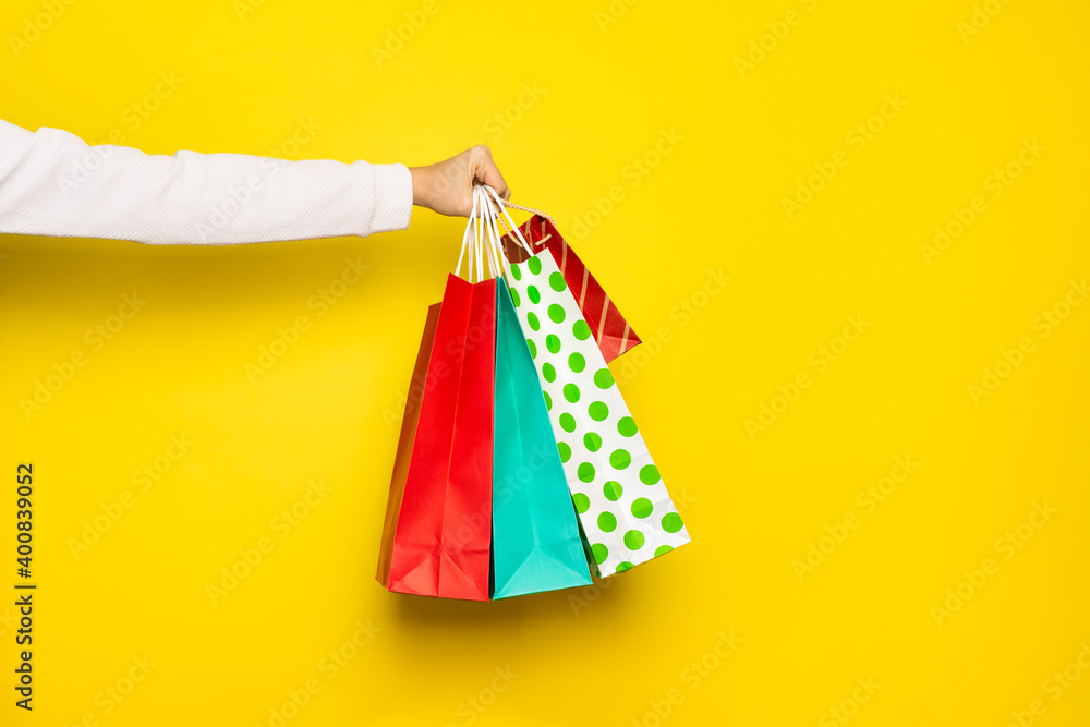 Shopping or sale concept. Female hand holds shopping paper bags isolated on yellow background.