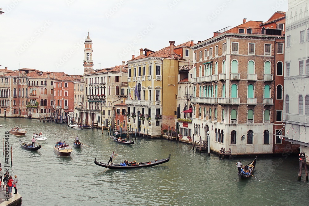 boat, gondola with tourists and a gondolier that steers the boat, green water and old Venetian buildings