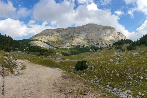 A gravelled road leading through Italian Dolomites. High, sharp mountains around. The slopes and meadow are green, higher parts barren and stony. Overcast. Remote and desolate place. Freedom photo