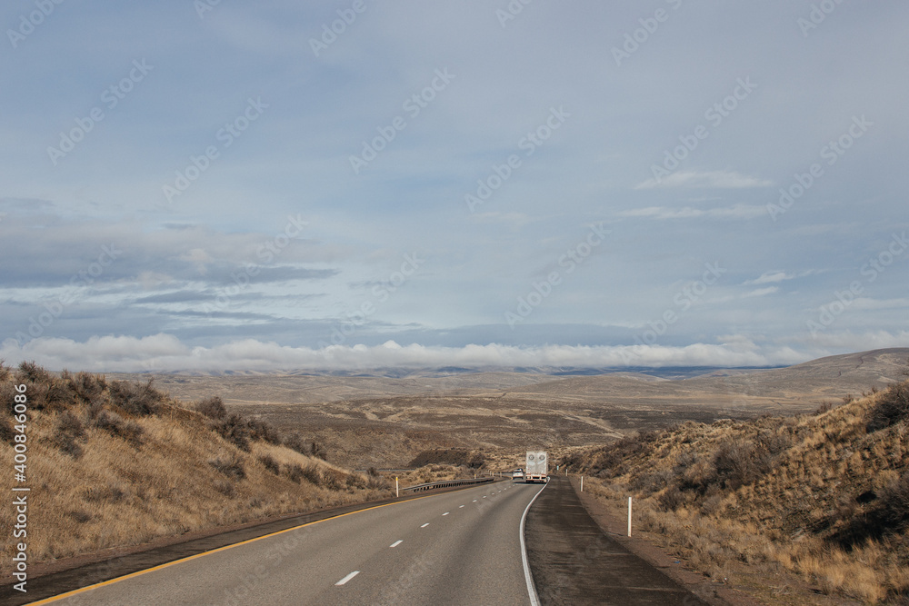 A beautiful landscape with a highway along which cars and trucks drive, on a sunny autumn day among the mountains, a blue sky with fluffy gray-blue clouds. Oregon, USA, 12-5-2019