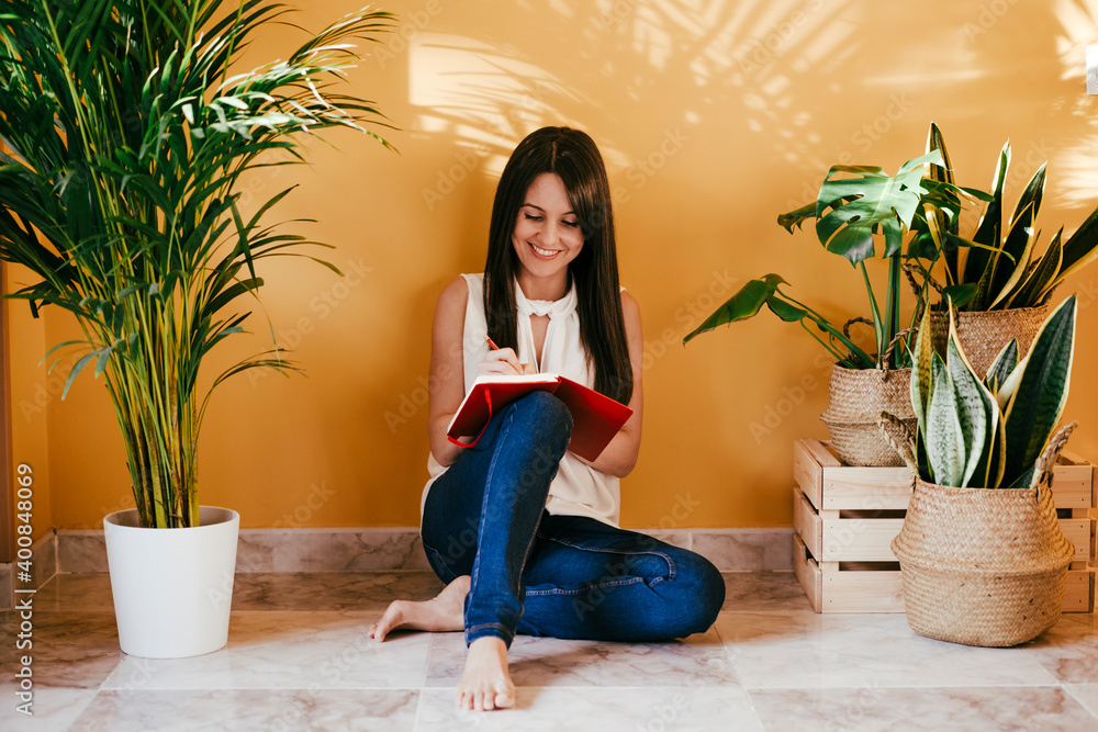 Woman writing in book while sitting on floor against yellow wall at home Woman writing in book while sitting on floor against yellow wall at home