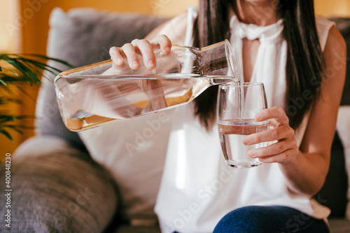 Woman pouring water from jar into drinking glass while sitting at home