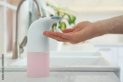 Man using automatic soap dispenser in kitchen  closeup