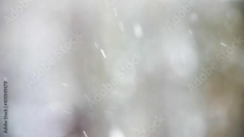 Video of a dreamy background of snow falling during a snowstorm with an out of focus forest in the distance.