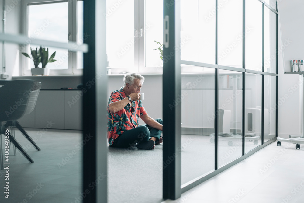 Businessman drinking coffee while sitting on floor at office Businessman drinking coffee while sitting on floor at office