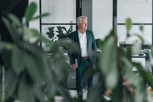 Businessman holding digital tablet looking away while standing at office