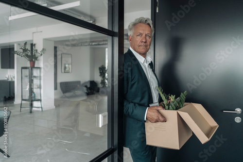Wallpaper Mural Businessman holding box of botany plant while leaning on glass wall at office Torontodigital.ca