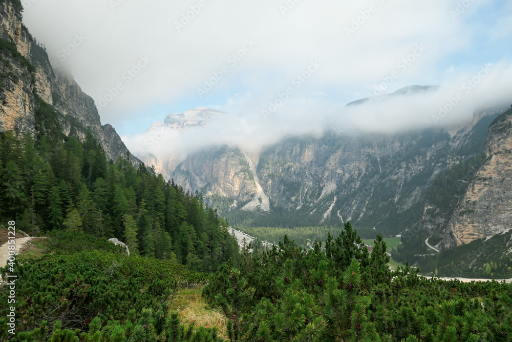 A panoramic view on a vast valley in Italian Dolomites. The bottom of the valley is very wide, covered with small pebbles. Sharp and tall mountains around, shrouded with thick clouds. Coming storm