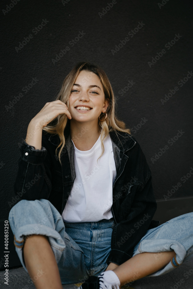 Smiling young woman sitting on footpath against wall Smiling young woman sitting on footpath against wall