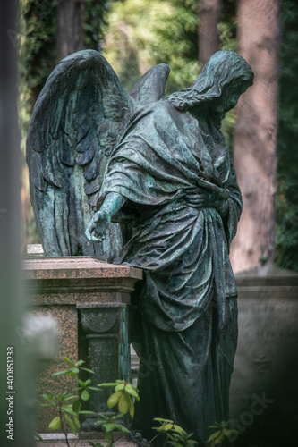 Weathered statue of angel standing beside tomb in cemetery