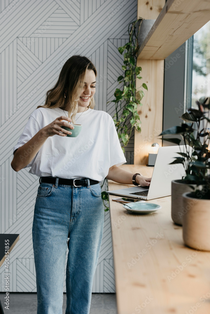 Young woman drinking coffee while working on laptop standing in cafe Young woman drinking coffee while working on laptop standing in cafe