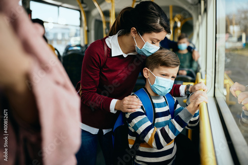 Caring mother and son with protective face masks traveling by public bus.