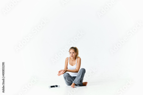 an athletic woman in a bright room sits on the floor and looks at dumbbells